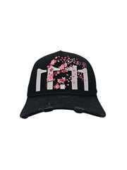 A front view of a black snapback baseball cap with hints of distressed texture and with embroidered pink floral blossom patterns between the 11.11 logo on a white backdrop.
