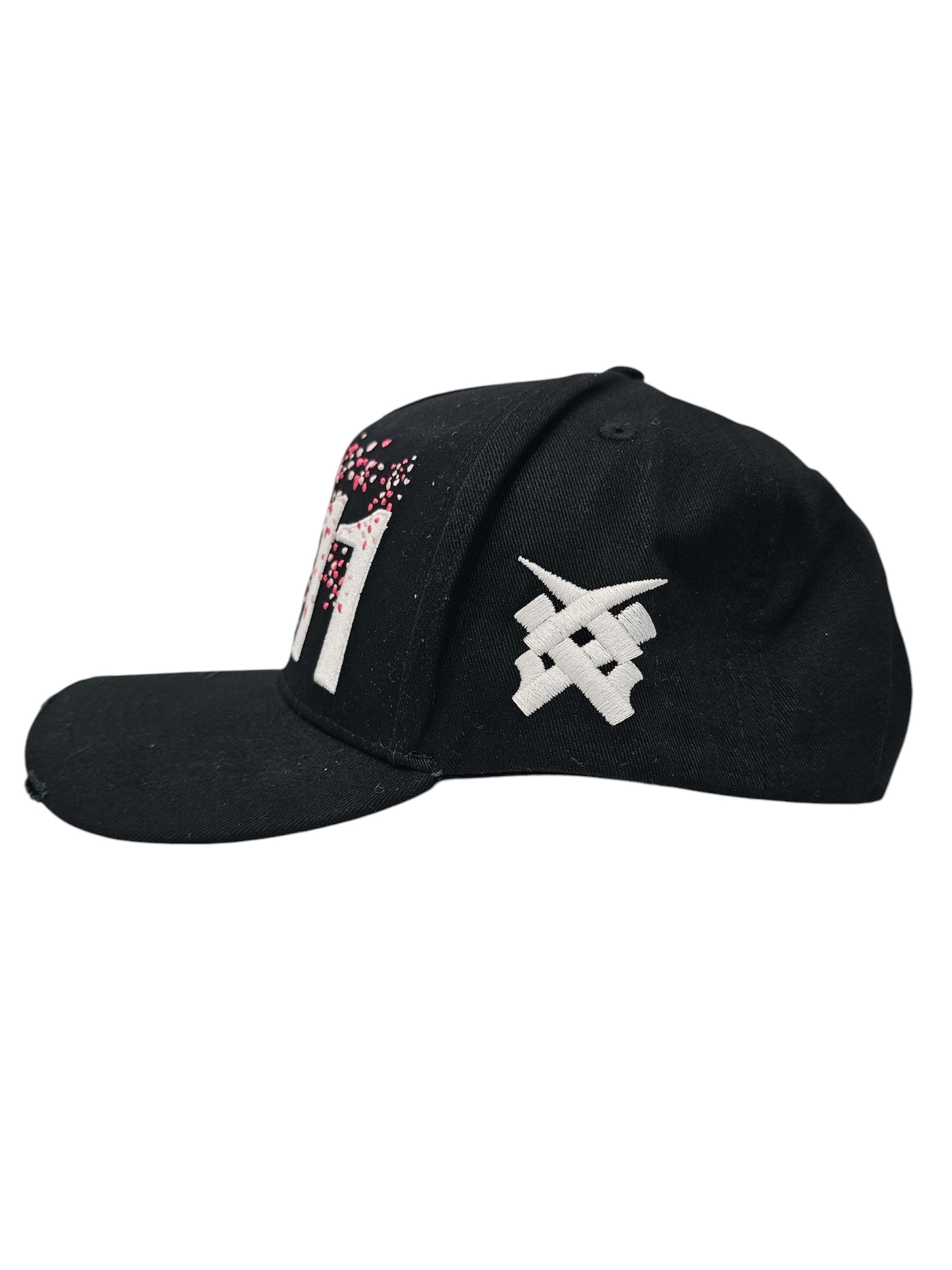 A right sided view of a black snapback baseball cap with hints of distressed texture and with embroidered pink floral blossom patterns between the 11.11 logo on a white backdrop. The right side of the cap has a white embroided 11.11 symbol logo on it
