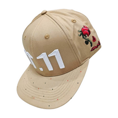 A floating right sided view of a beige snapback baseball cap with an embroidered white 11.11 number logo, also revealing The Broken Roses Illustration on the right side of the cap on a white backdrop.