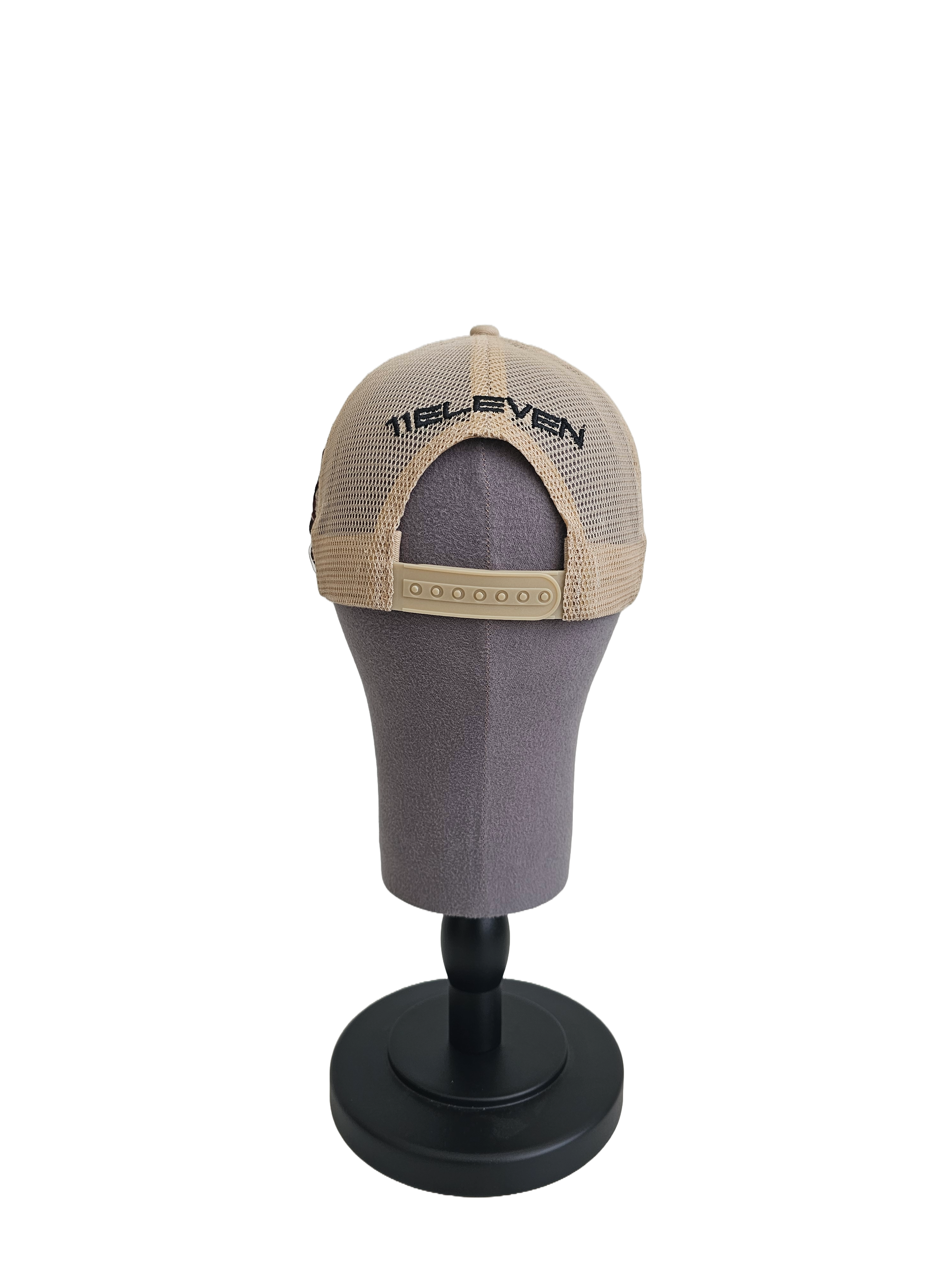 A back view of a beige snapback trucker cap on a mannequin head with an embroidered black 11.11 logo on a mesh trucker snapback cap with an adjustable cap strap