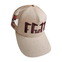 A left angled floating view of a beige snapback trucker cap with an embroidered brown 11.11 number logo. The left side of the cap reveals the Broken Rose illustration on the trucker mesh cap on a white backdrop.
