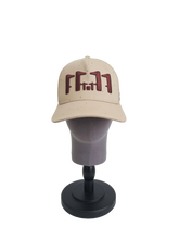 A front view of a beige snapback trucker cap on a mannequin head with an embroidered brown 11.11 number logo