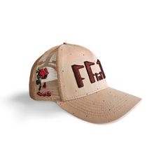 A left angled view of a beige snapback trucker cap with an embroidered brown 11.11 number logo. The left side of the cap reveals the Broken Rose illustration on the trucker mesh cap on a white backdrop.