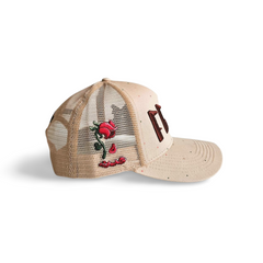 A left sided view of a beige snapback trucker cap with an embroidered brown 11.11 number logo. The left side of the cap reveals the Broken Rose illustration on the trucker mesh cap on a white backdrop.