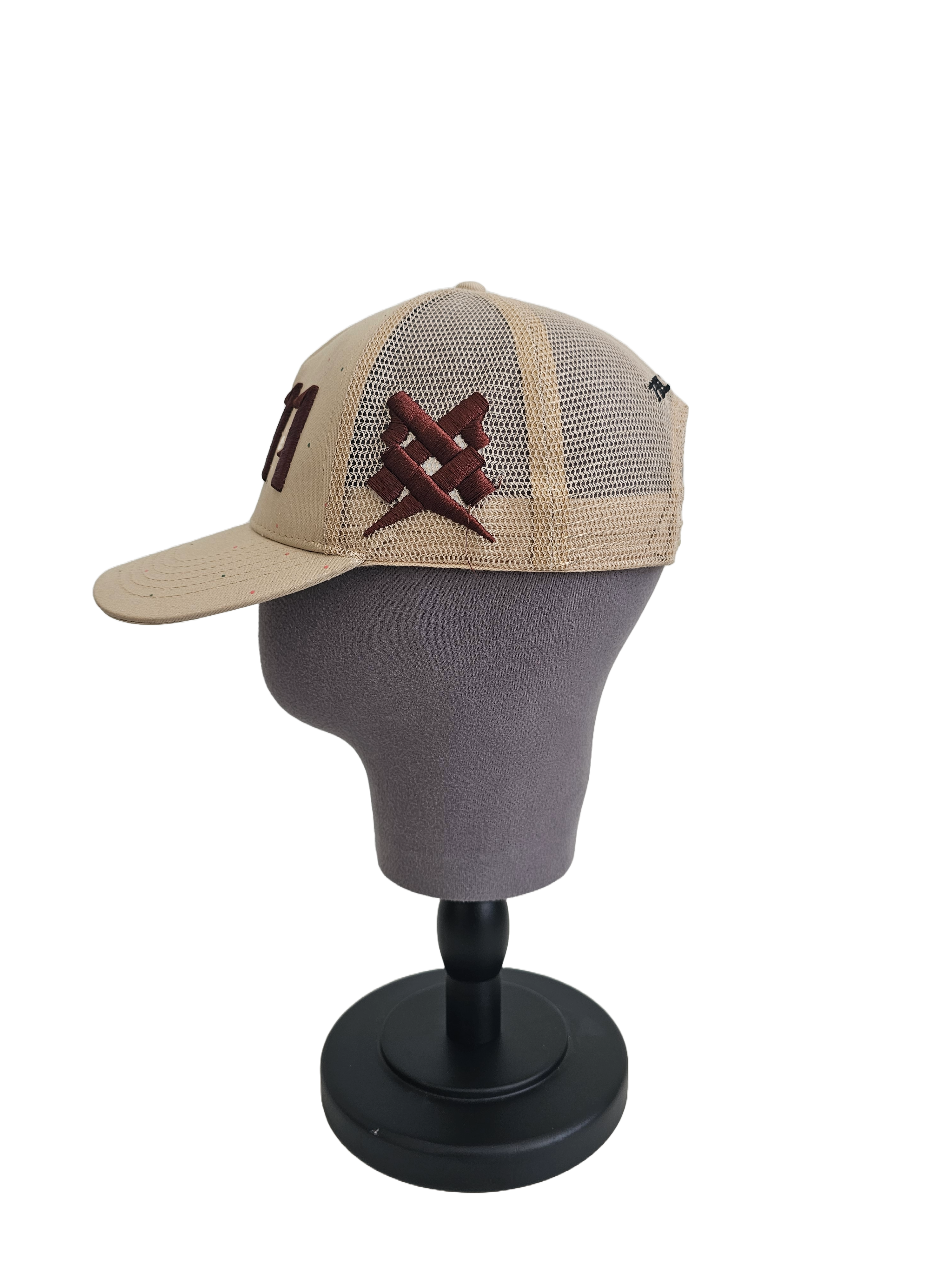 A right sided view of a beige snapback trucker cap on a mannequin head with an embroidered brown 11.11 number logo. The right side of the cap reveals a brown embroidered 11ELEVEN symbol logo on the trucker mesh cap