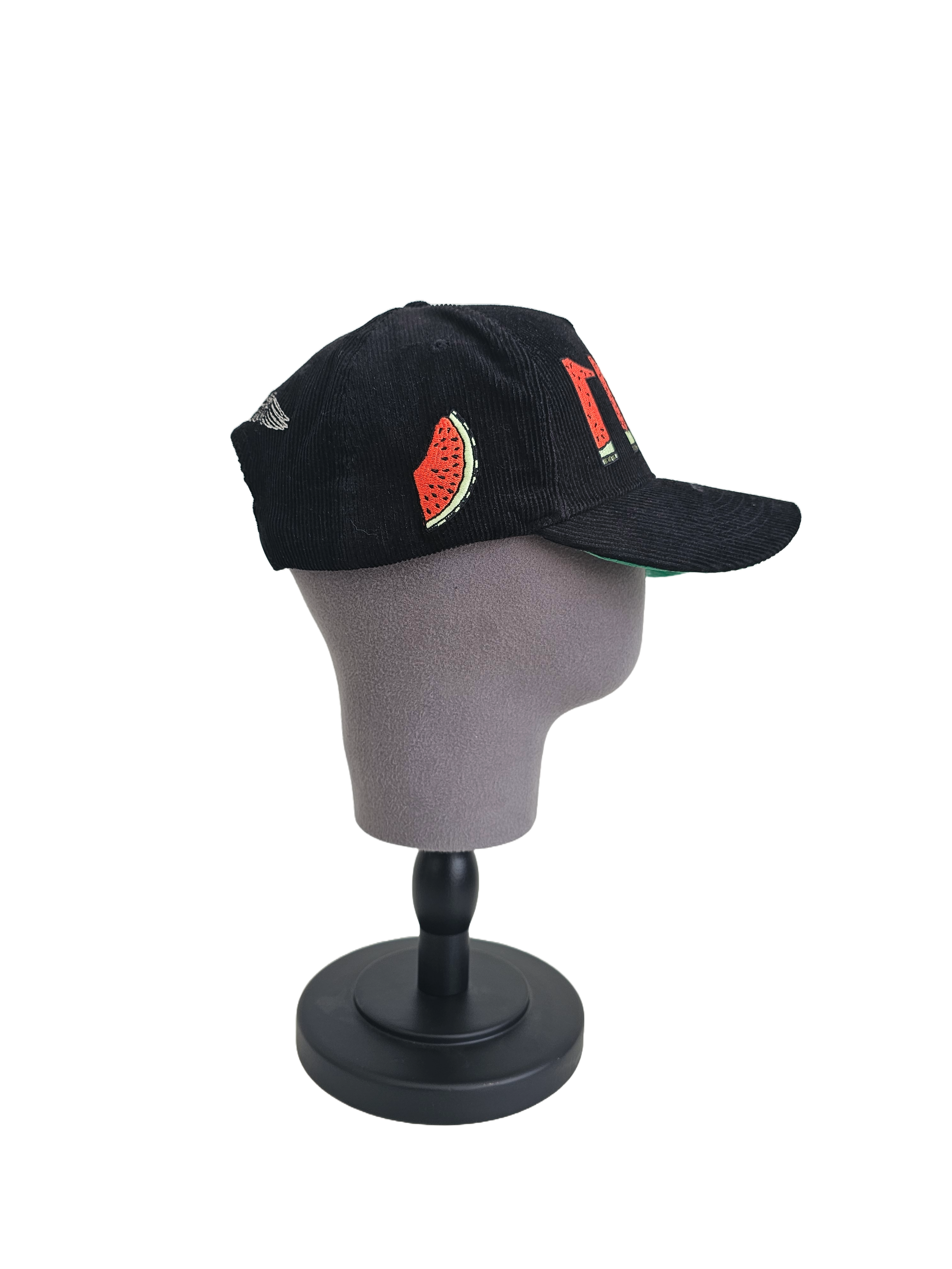 Side view of black corduroy snapback hat with embroidered 11:11 logo and watermelon slice in the shape of the Palestinian land, pro-Palestine streetwear cap symbolizing solidarity, featuring red, green, white, and black accents.