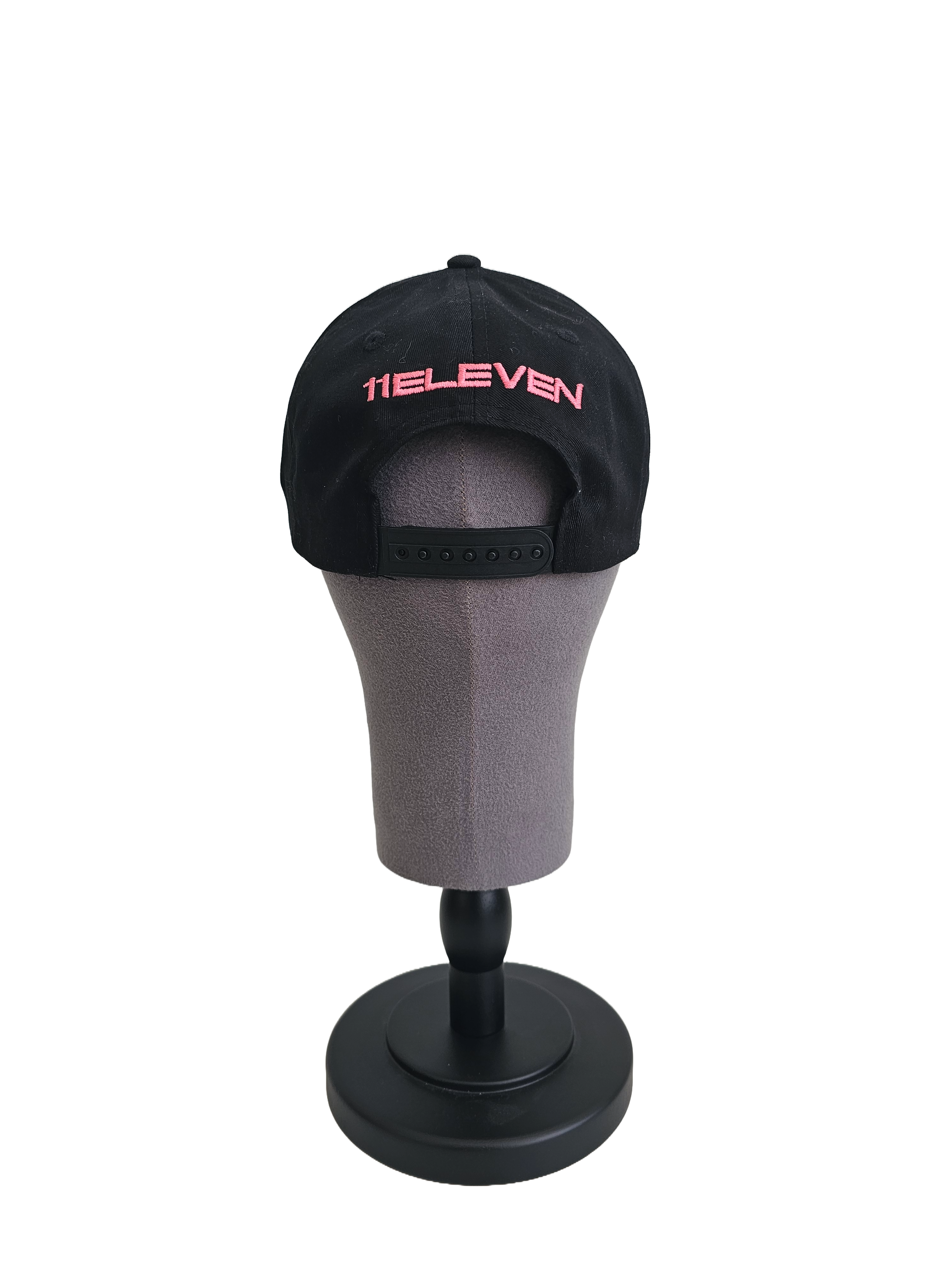 A back view of a black snapback baseball cap on a mannequin head with hints of distressed texture and with embroidered pink 11.11 logo on a white backdrop. The cap also shows the adjustable snapback cap strap.