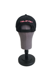 A back view of a black snapback baseball cap on a mannequin head with hints of distressed texture and with embroidered pink 11.11 logo on a white backdrop. The cap also shows the adjustable snapback cap strap.