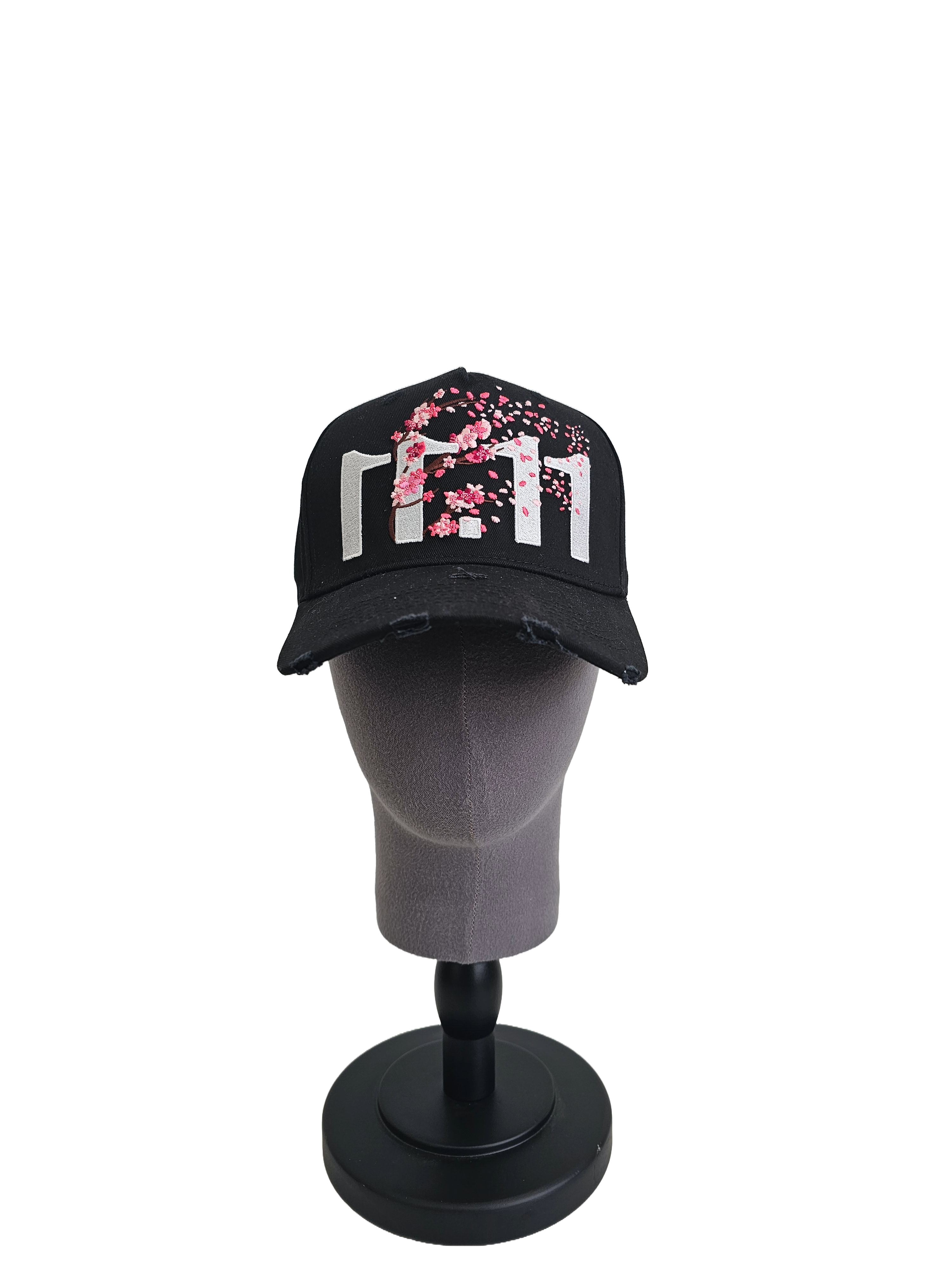A front view of a black snapback baseball cap on a mannequin head with hints of distressed texture and with embroidered pink floral blossom patterns between the 11.11 logo on a white backdrop.