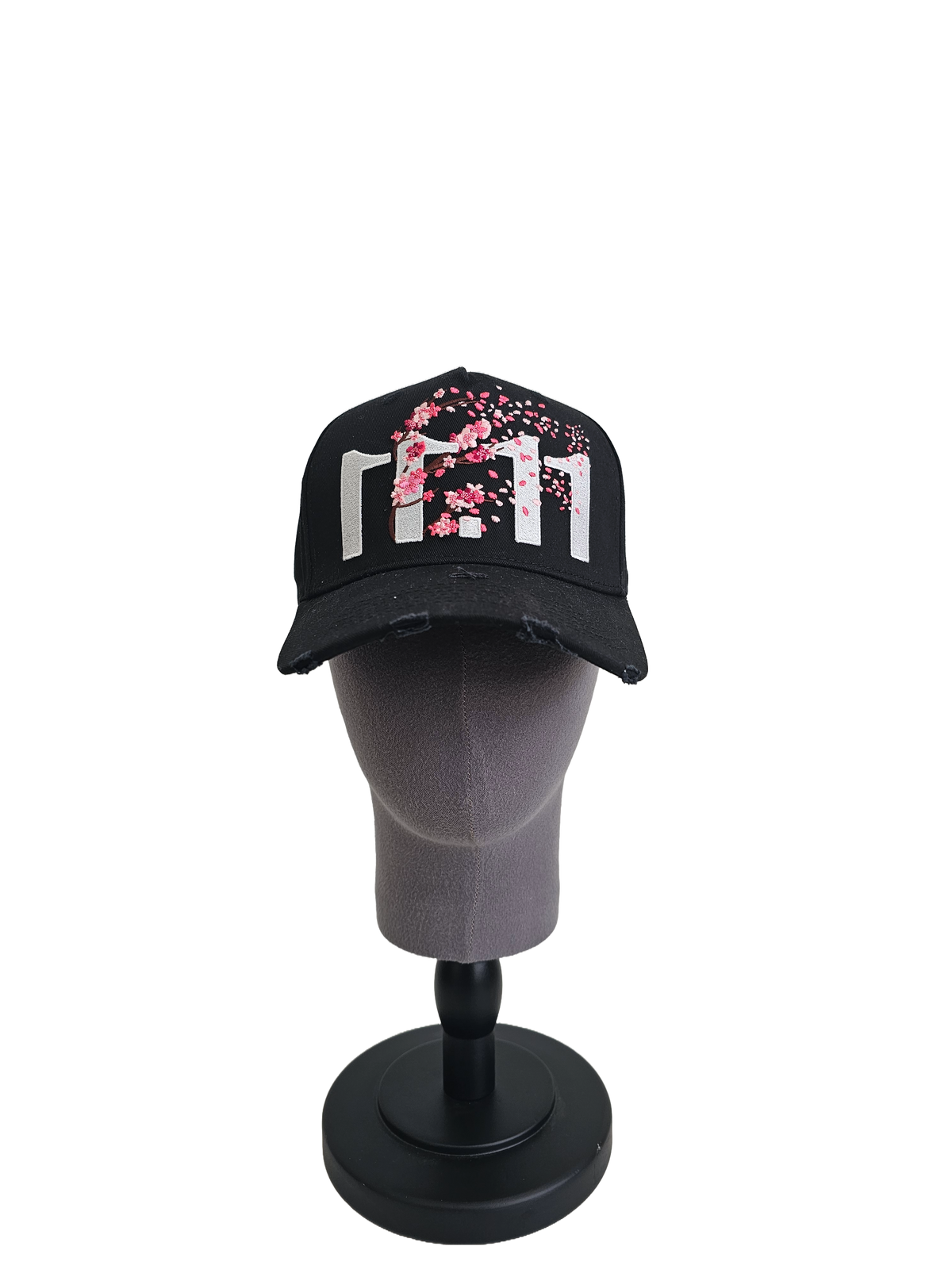 A front view of a black snapback baseball cap on a mannequin head with hints of distressed texture and with embroidered pink floral blossom patterns between the 11.11 logo on a white backdrop.