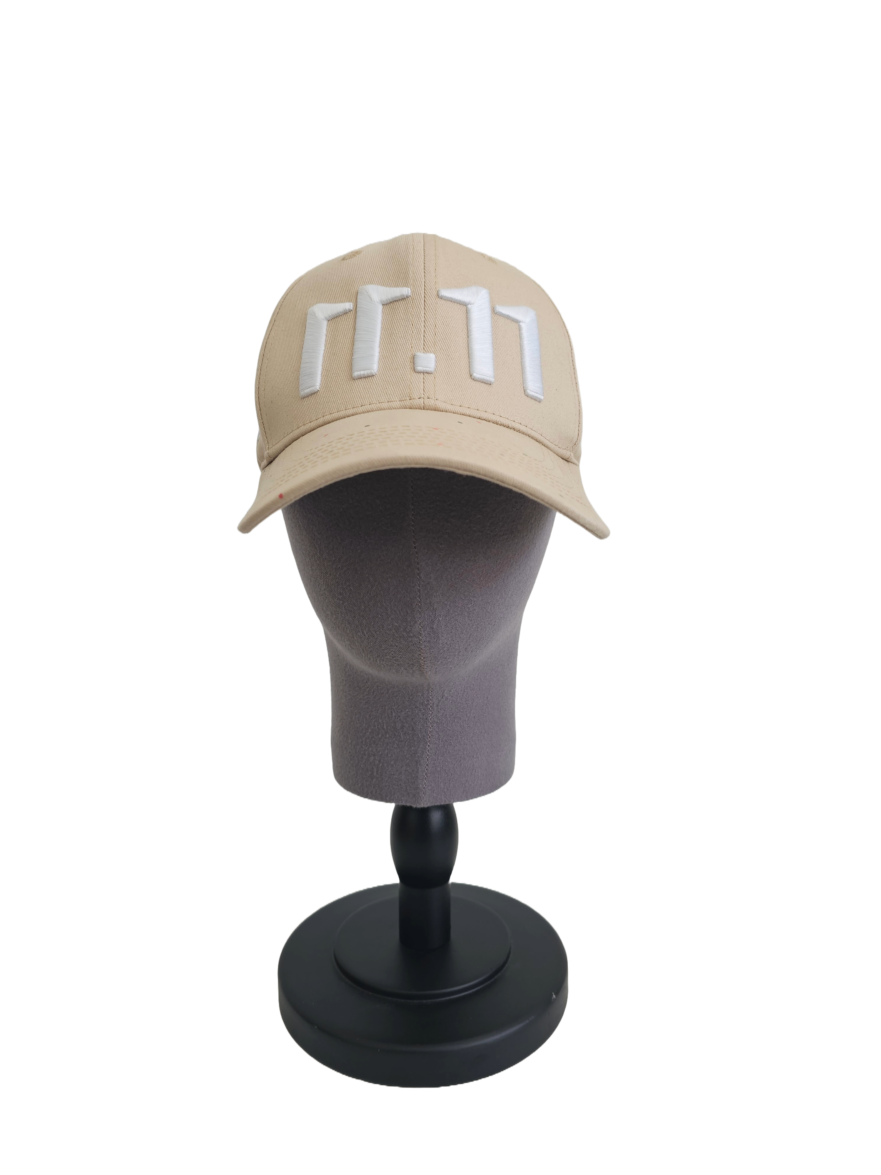 A front view of a beige snapback baseball cap on a mannequin head with an embroidered white 11.11 number logo