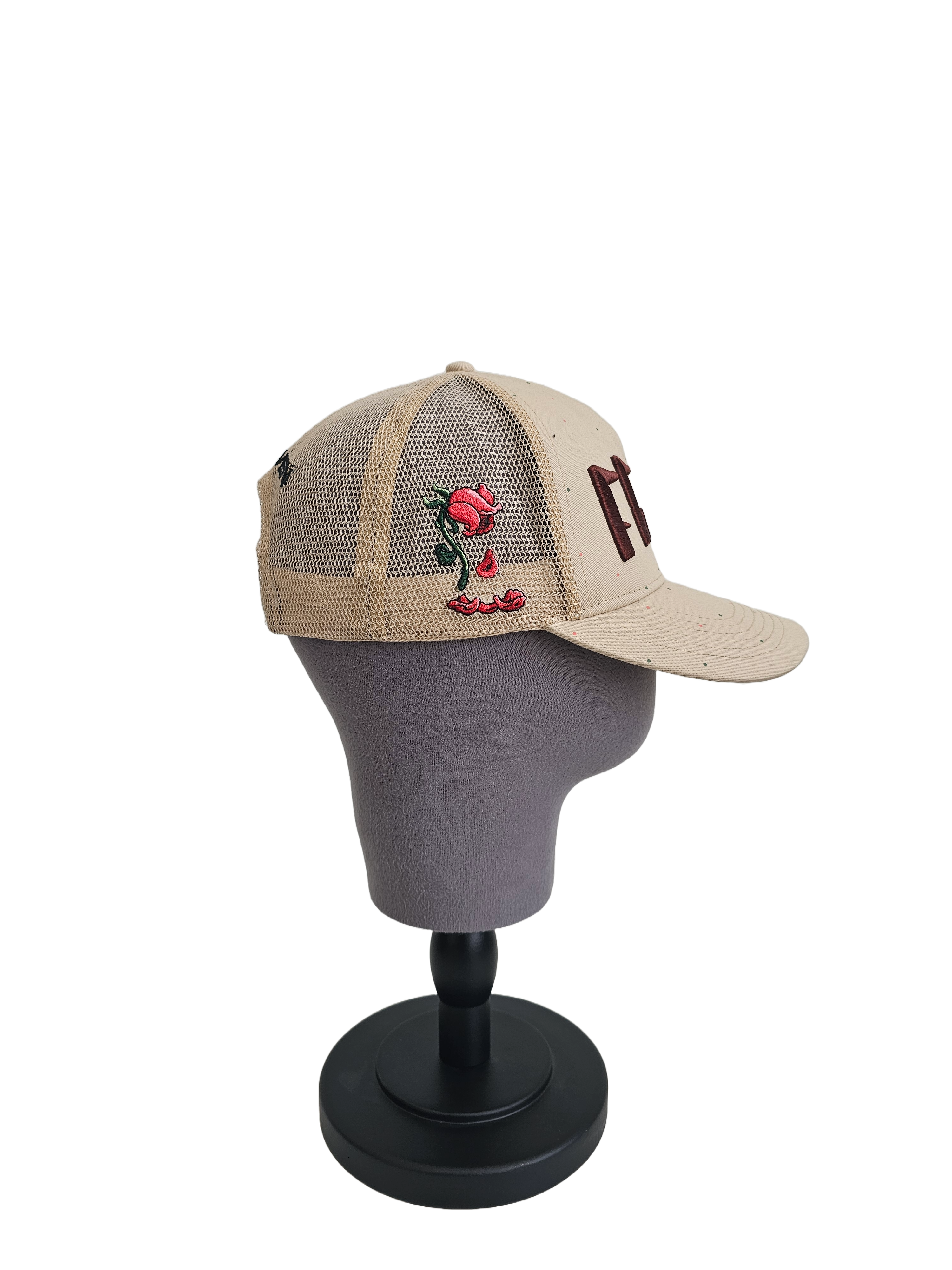 A left sided view of a beige snapback trucker cap on a mannequin head with an embroidered brown 11.11 number logo. The left side of the cap reveals the Broken Rose illustration on the trucker mesh cap